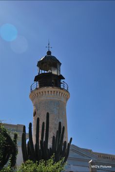 a tall tower with a light on top and cactus in the foreground against a blue sky