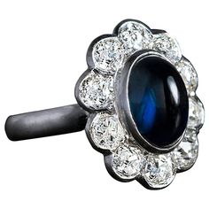 Mid century, circa 1950s A platinum cluster ring is bezel-set with a cabochon cut midnight blue sapphire surrounded by ten sparkling old mine cut diamonds, H-I-J color, VS1-SI1 clarity. Total diamond weight 2.43 Ct Sapphire 4.15 Ct Sapphire and diamond cluster measures 19 x 16 mm (3/4 x 5/8 in.) Ring size 6.75 (17 mm) sizable Art Nouveau Engagement Ring, Morganite Engagement Ring Vintage, Pink Engagement Ring, Bezel Set Engagement Ring, Pink Sapphire Ring Engagement, Rose Gold Engagement Ring Vintage, Diamond Sapphire Engagement Ring, Sapphire Diamond Engagement, Cute Engagement Rings