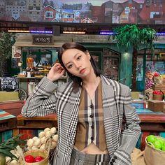 a woman standing in front of a table filled with fruits and vegetables, wearing a plaid blazer