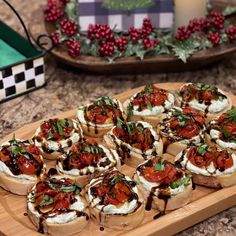 small appetizers with tomatoes and cream cheese on a wooden platter next to holly wreaths