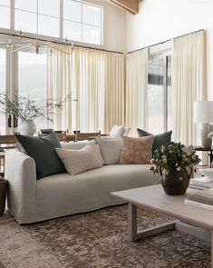 a living room filled with lots of furniture and large windows covered in white drapes