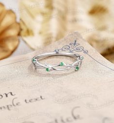 a silver ring with green stones sitting on top of a piece of paper