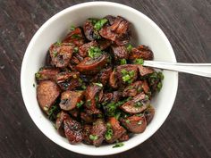 a white bowl filled with cooked mushrooms and green onions on top of a wooden table