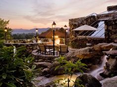 an outdoor dining area with tables, chairs and umbrellas next to a waterfall at sunset