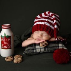 a baby wearing a red and white knitted hat is sleeping next to cookies and milk