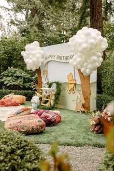 an outdoor birthday party with balloons and stuffed animals on the grass in front of a sign