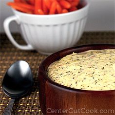 a wooden bowl filled with food next to a white bowl full of carrots and a spoon