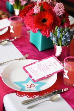 the table is set with pink and red flowers, silverware, and place settings