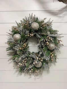 a christmas wreath hanging on the side of a white wall with pine cones and silver ornaments