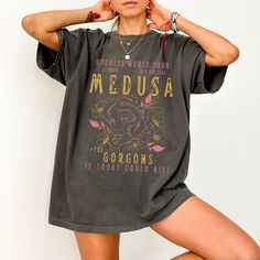 Get ready to be OBSESSED with your new Medusa shirt. It's the cutest and most trendy way to combine all those important trendy Greek Mythology, feminism and light academia vibes! This is the perfect snake shirt!  * Q U I C K * F A C T S * ✺  All shirts are UNISEX ✺  100%  ringspun cotton (fiber content may vary for different colors) ✺  Soft-washed, garment-dyed fabric brings extra coziness ✺  Wash and dry normally (on cool for best results) ✺  Sewn-in twill label * S I Z I N G * ✺ For an oversized fit, select two or three sizes up from your normal size ✺ Model is wearing size L  ✺ Sizing runs true to size ✺ Relaxed fit ✺ Most women find their typical size works best, since they are meant to fit a touch loose ✺ See Size guide and fit in images          * S H I P P I N G * T I M E S * ✺ Our Fairy Grunge Crew Neck Top With Letter Print, Fairy Grunge Crew Neck T-shirt Relaxed Fit, Fairy Grunge Relaxed Fit Crew Neck T-shirt, Goblincore Graphic Print Short Sleeve T-shirt, Fairy Grunge Short Sleeve Top With Relaxed Fit, Fairy Grunge Relaxed Fit Short Sleeve Tops, Cotton Short Sleeve Goblincore T-shirt, Goblincore Short Sleeve T-shirt For Summer, Fairy Grunge Cotton Tops With Letter Print