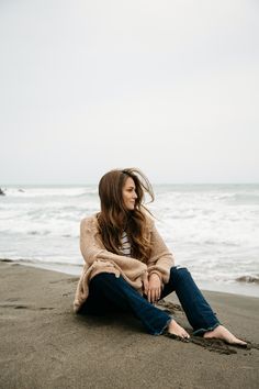 a woman sitting on the beach with her hair blowing in the wind