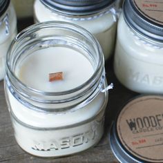 several jars filled with white candles sitting on top of a wooden table next to each other