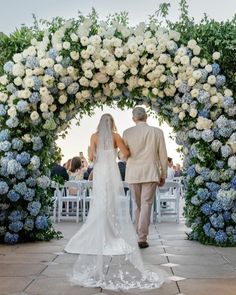 a bride and groom walking down the aisle at their wedding ceremony in front of an arch of flowers