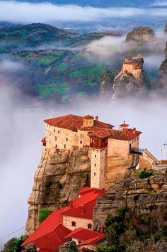 an old castle perched on top of a cliff surrounded by fog and mist in the mountains