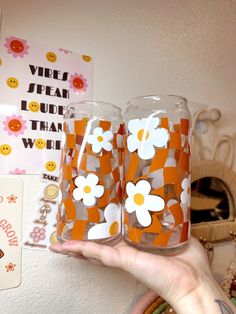 two glasses with flowers painted on them are being held up by a woman's hand