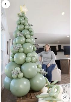 a woman sitting next to a christmas tree made out of balloons