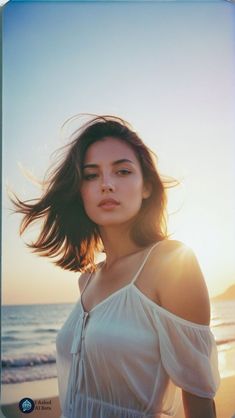 a woman standing on top of a beach next to the ocean with her hair blowing in the wind