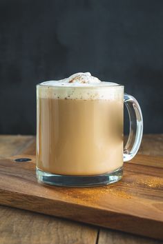 there is a cup of coffee with whipped cream in it on a wooden table next to a cutting board