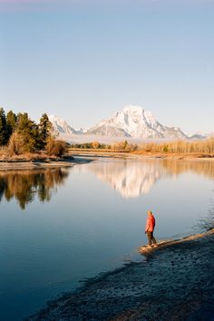 a person standing on the shore of a lake in front of snow capped mountain range