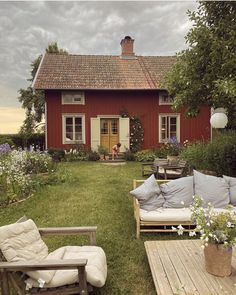 a red house with two couches in front of it and flowers on the lawn