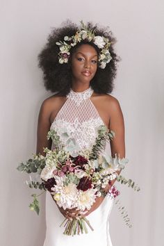 a woman in a white wedding dress holding a bouquet of flowers and greenery on her head