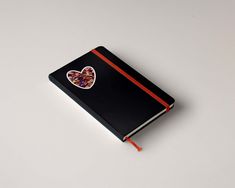 a black notebook with a heart shaped sticker on the front and red stripe around the cover