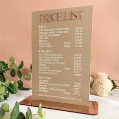 a price list sign sitting on top of a table next to flowers and greenery