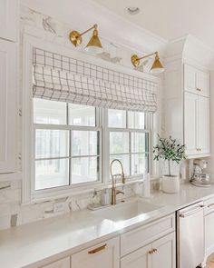 a kitchen with white cabinets and marble counter tops, gold faucet lights above the sink