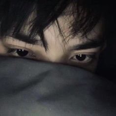 a man hiding his face behind the covers with his eyes wide open and looking at the camera