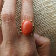 This beautiful Mid-Century cocktail ring features a cabochon cut red coral in 18 karat yellow gold. The coral has a medium scarlet red hue and is set in four golden prongs. The shoulders of the tapered band feature streamlined, openwork spaces for a bit of skin to peek through. From the profile, the Mid-Century details of the ring can truly be admired. The ring has a strong architecture and distinct style, finished in high polish 18k yellow gold. PRIMARY STONE Stone: Natural Red Coral Measuremen Formal Orange Cabochon Ring, Elegant Oval Coral Rings, Elegant Coral Oval Rings, Formal Coral Ring, Formal Yellow Gold Jewelry With Red Coral, Modern Jewellery Design, Right Hand Ring, Vintage Cocktail Ring, Right Hand Rings