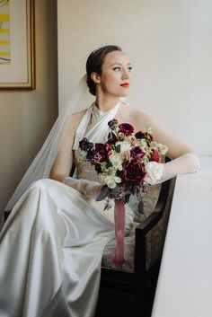 a woman in a wedding dress sitting on a chair holding a bridals bouquet