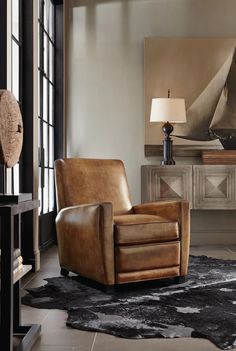 a brown leather chair sitting on top of a rug in front of a table with a lamp