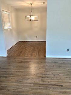 an empty living room with hard wood floors and white walls, light fixture hanging from the ceiling