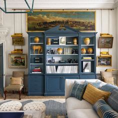 a living room with blue bookcases and paintings on the wall above it's fireplace