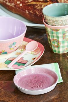 there are plates, cups and spoons on the table with bread in the background