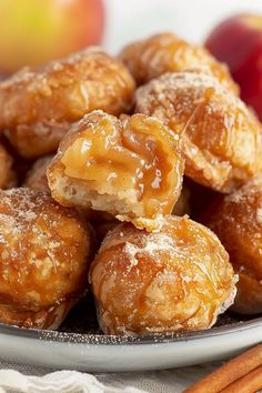 some sugar covered donuts on a plate with cinnamon sticks and an apple in the background