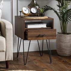 an end table with two clocks on top and some plants in the corner next to it