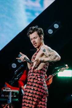 a man with tattoos on his arm holding a microphone and standing in front of a stage