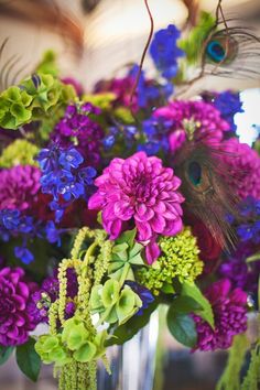 a vase filled with lots of purple and green flowers next to a peacock feather on top of it