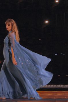 a woman is walking down the runway in a blue dress with long sleeves and flowing skirt