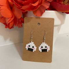 a pair of earrings with sheeps on them sitting next to a red flower pot