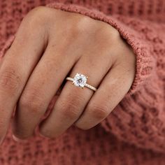 a woman's hand with a diamond ring on her finger and a pink sweater