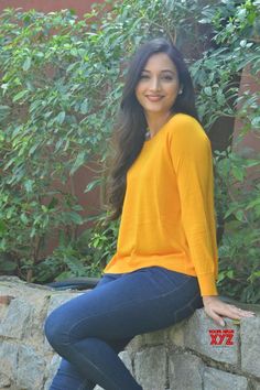 a beautiful young woman sitting on top of a stone wall