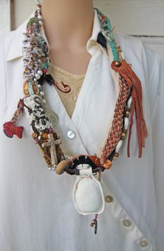 This large lightweight fabric and leather necklace is new, handmade, and one of a kind.  It slips easily over the head and is 34" around, made of different fabrics and textiles, suede and leathers.  I beaded this necklace with beads made of wood, bone, shells, cowry shells, brass, glass, plastic, and faux pearls. I added a black bow charm, a silver charm with a branch impression, a flying dove, and a painted vintage Mexican fish charm. There is also a small wooden cross, woven beaded leather, and a white leather fob that I made after looking at rustic African Akan jewelry from about 1950. This necklace is photographed being worn by a lifesize mannequin, and also next to a ruler. It is new and was made in a smoke-free environment. It has a very eclectic Bohemian feel, and looks elegant when Bohemian Leather Necklace For Festivals, Mexican Fish, Flying Dove, Leather Fob, Textile Necklace, Bohemian Festival, Fabric Necklace, Festival Jewelry, Wooden Cross