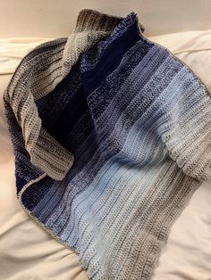 a blue and white blanket laying on top of a bed next to an unmade pillow