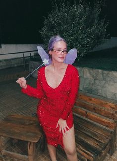 a woman in a red sequin dress sitting on a bench with a fairy wand