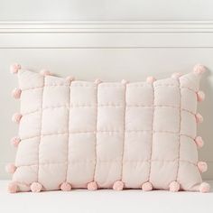 a white pillow with pink pom - poms on the front and back of it