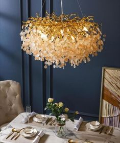 a chandelier hanging over a dining room table with place settings and flowers on it