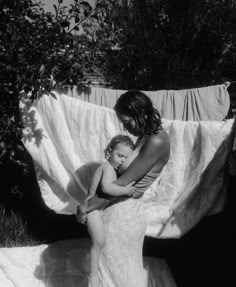 a woman holding a baby in her arms while standing next to a white cloth covered area