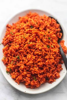 a white plate topped with carrot rice and a spoon